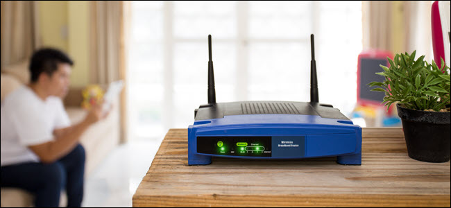 A wireless router on a table and a blurred young man using a tablet in the background.