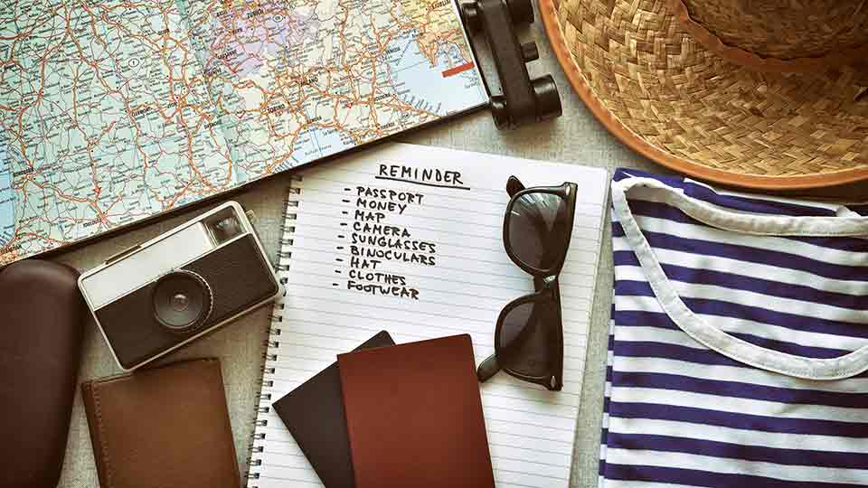 travel packing list, surrounded by travel items like a camera, sun hat, and map