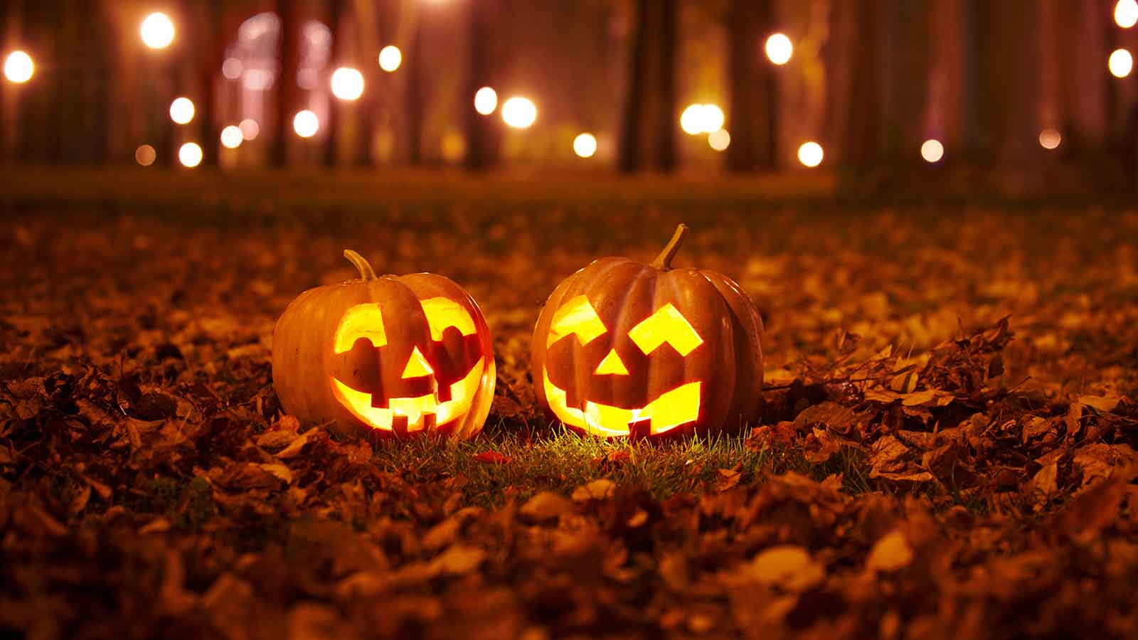 Two carved jack-o'-lanterns sitting outside on a bed of leaves.