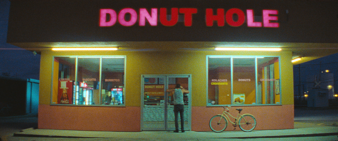 Man peers into darkened donut shop. 