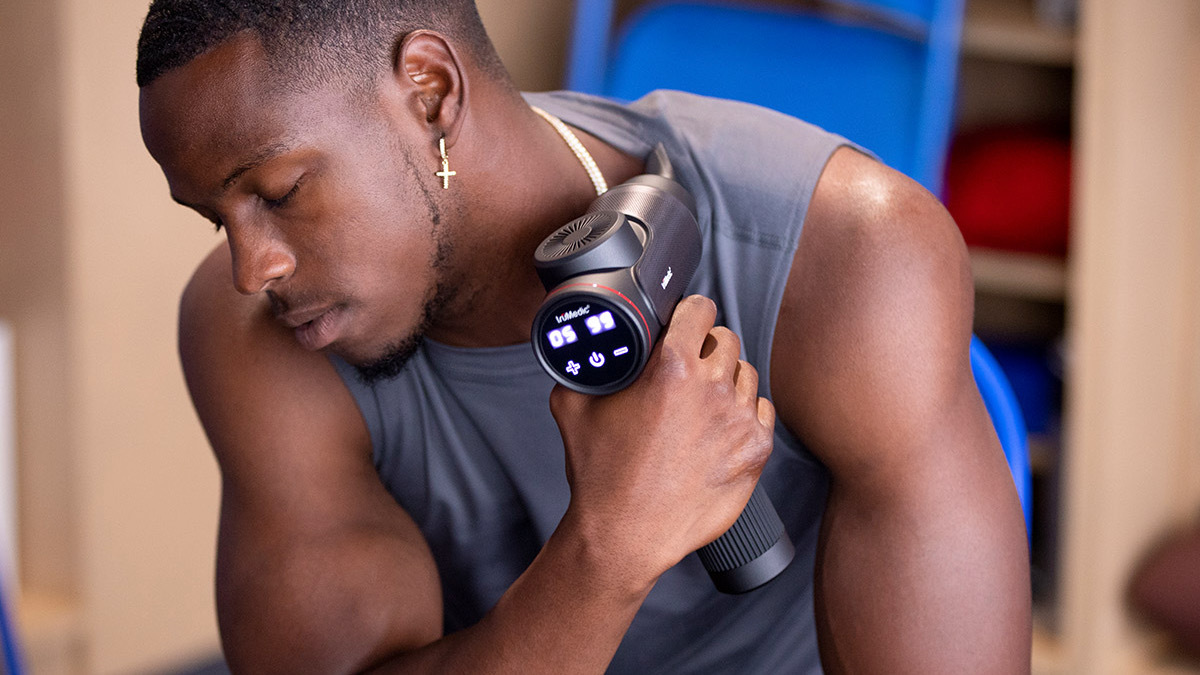 Person using massage gun with lit-up display on shoulder