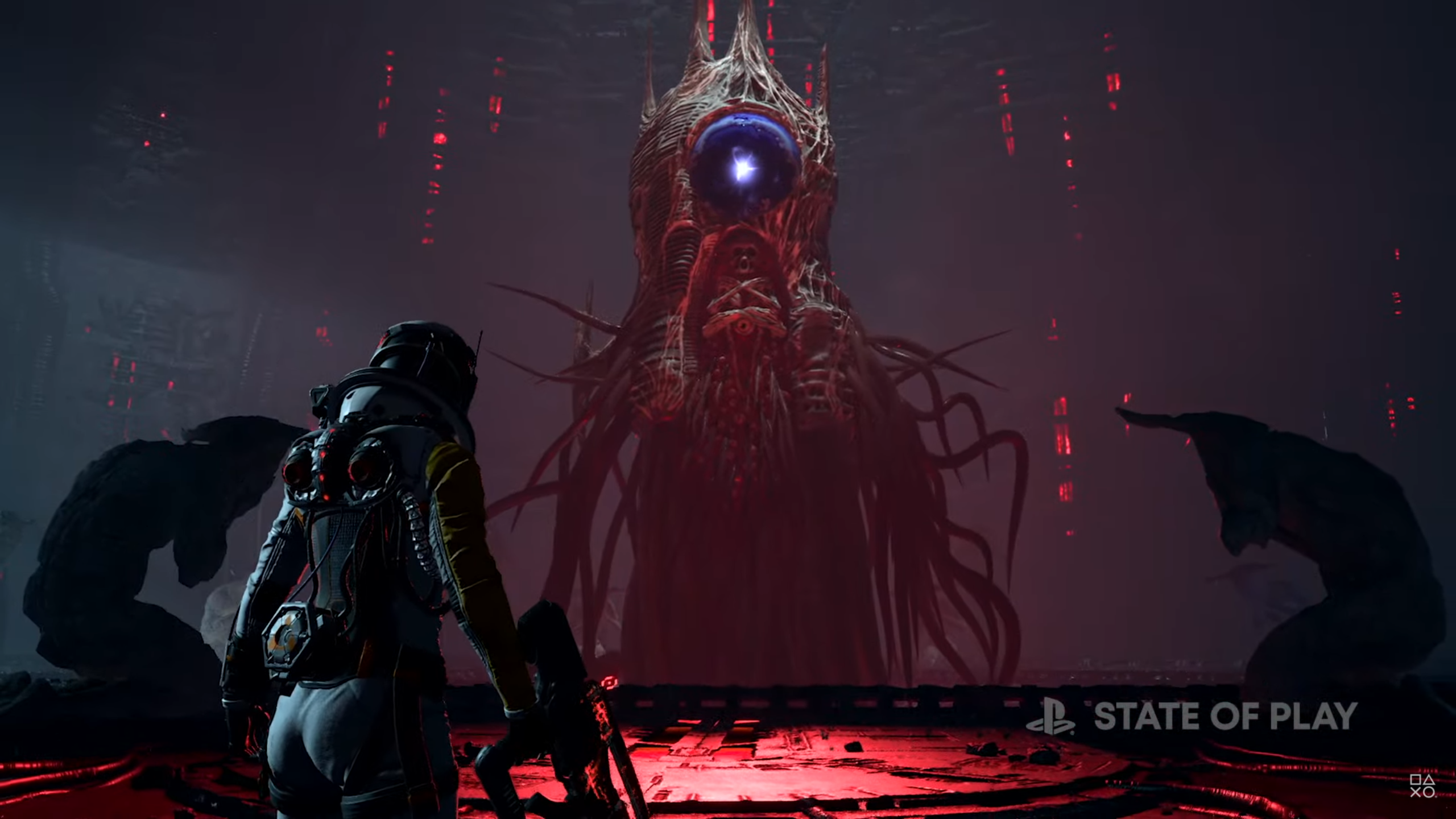 A screenshot from the PlayStation game Returnal. A woman in a futuristic space suit stands in a creepy, alien chamber looking at a large, pillar-like creature that's all bones, tentacles, and sharp, pointy spikes.