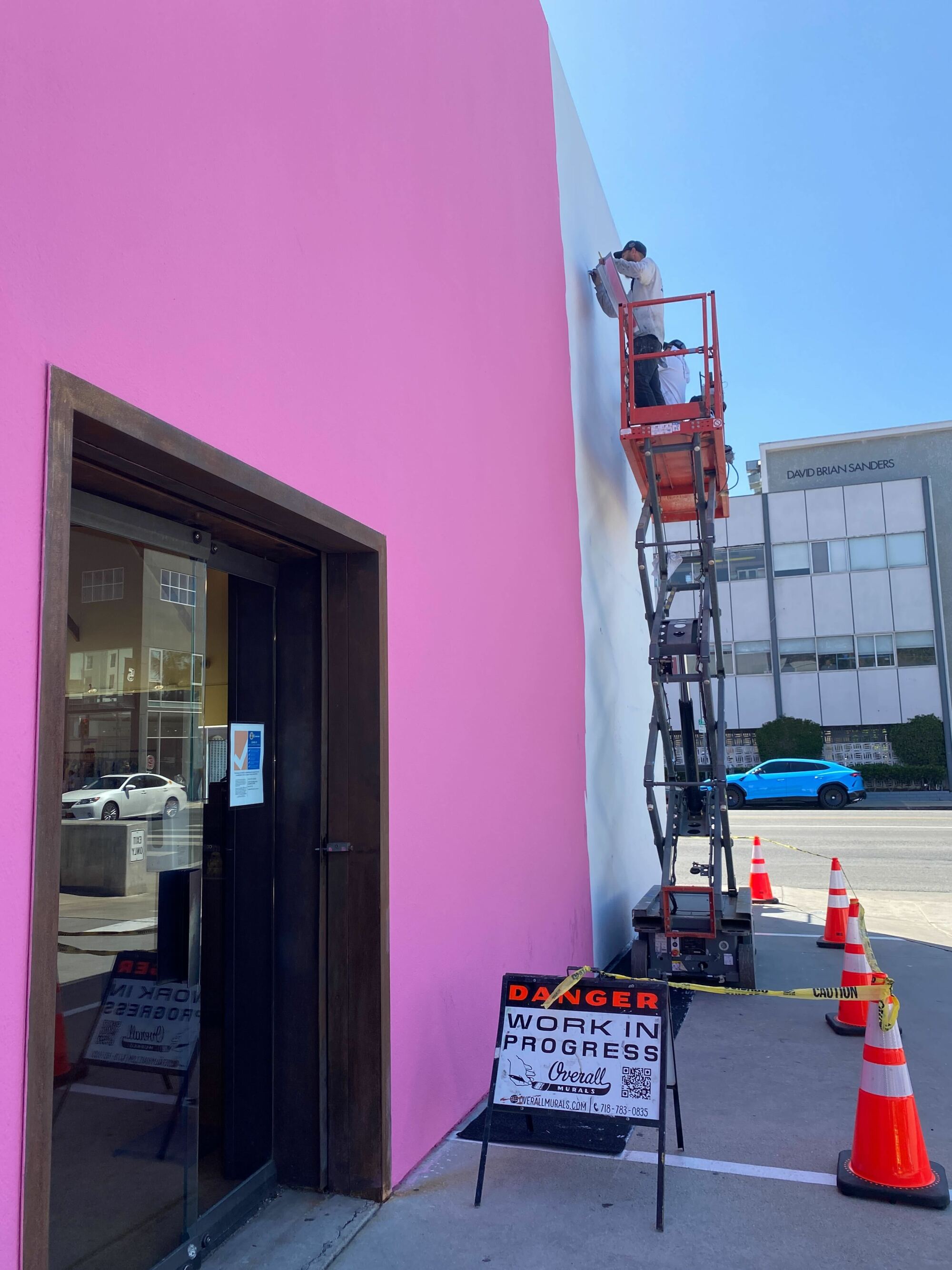 Painters next to a pink wall with a sign that says Danger: Work In Progress.