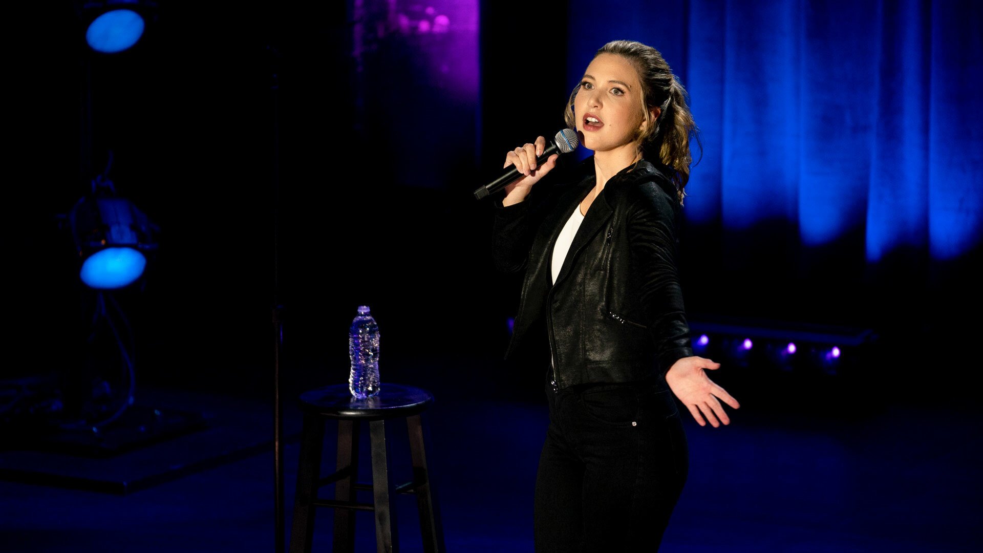 Taylor Tomlinson holding a microphone on a stage in her Netflix special, "Quarter-Life Crisis."