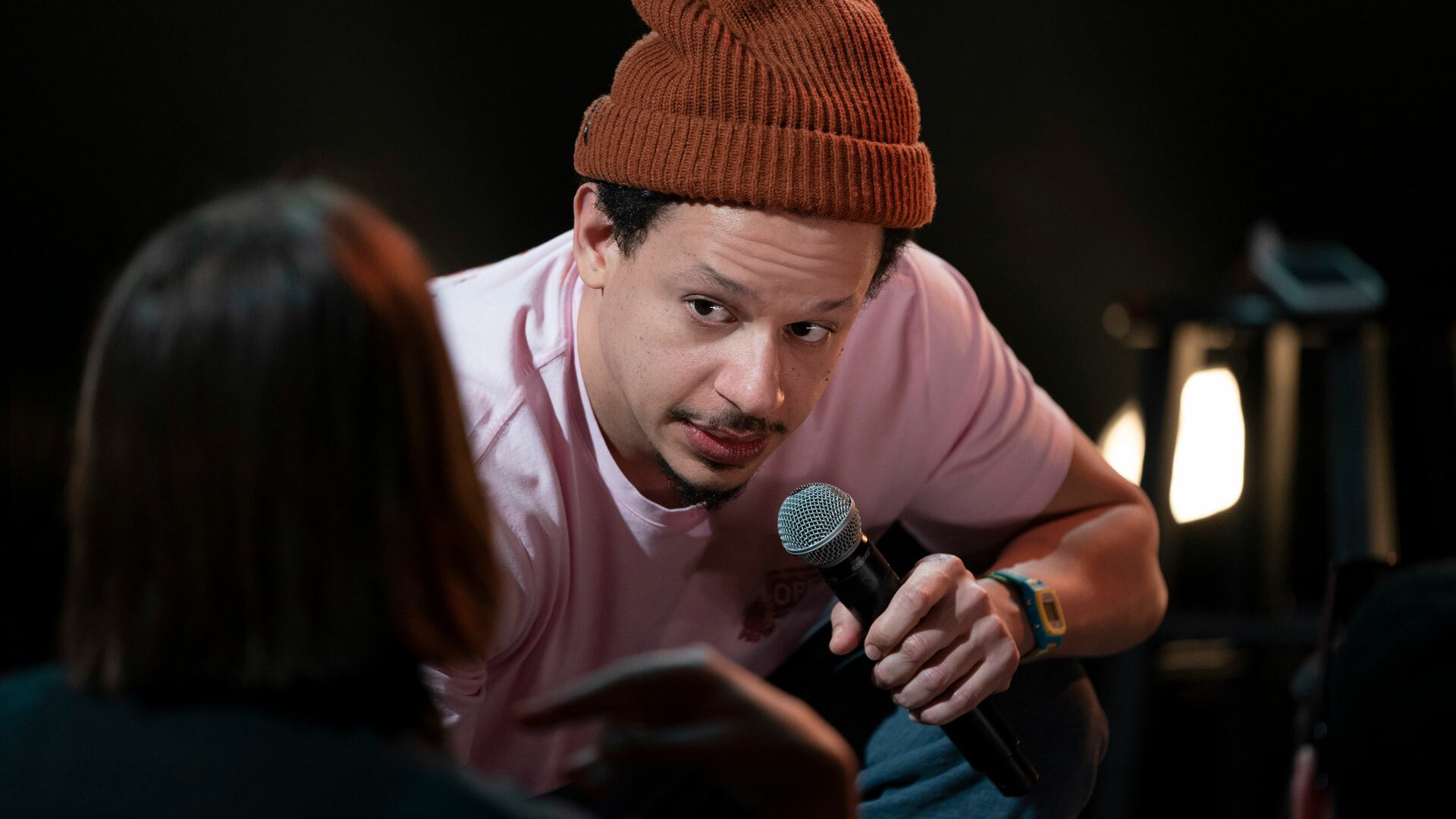 A close-up of Eric Andre as he holds a microphone and talks to a fan, who we see from behind, up close.