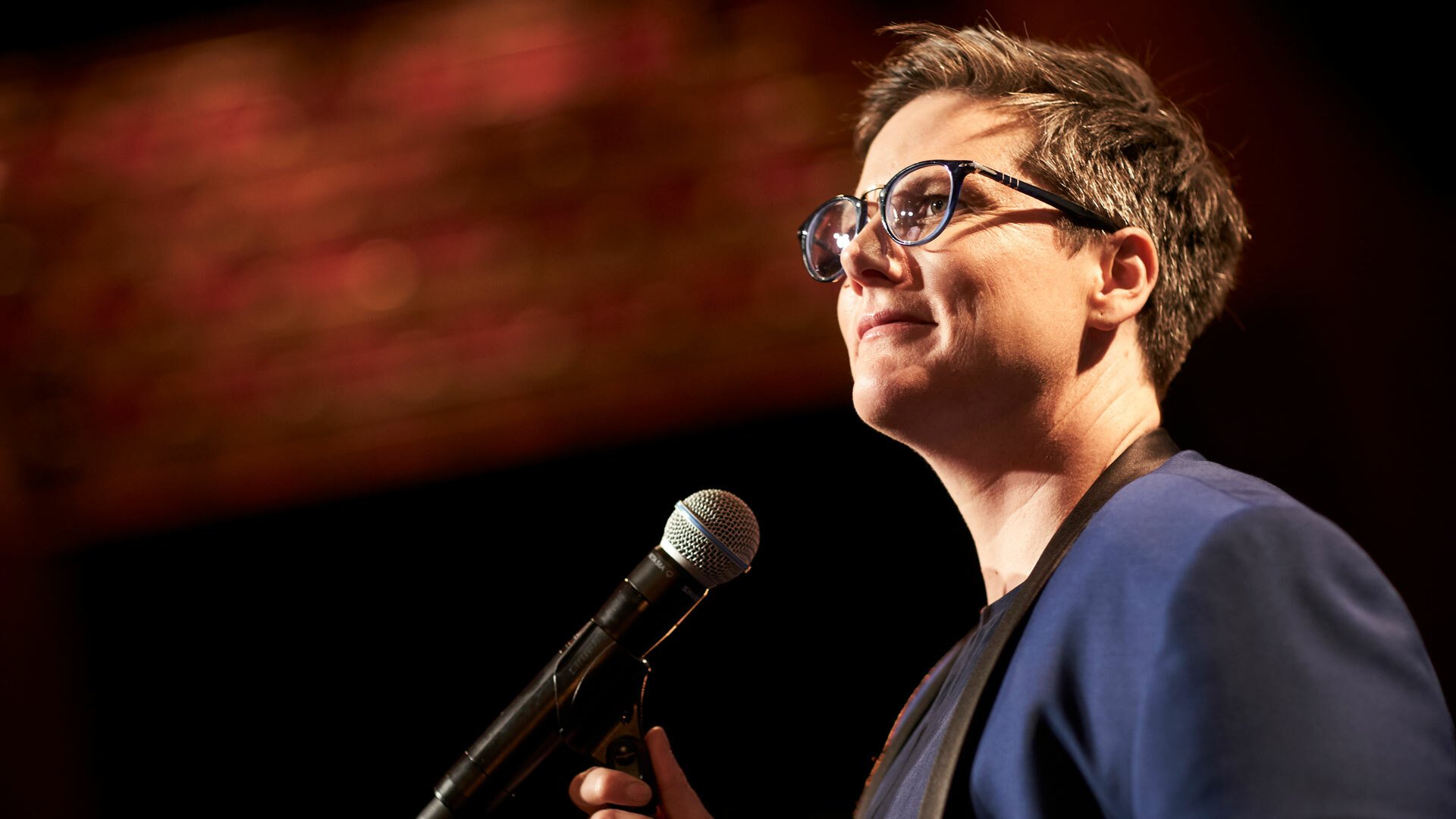 A close-up of Hannah Gadsby standing in front of a microphone.